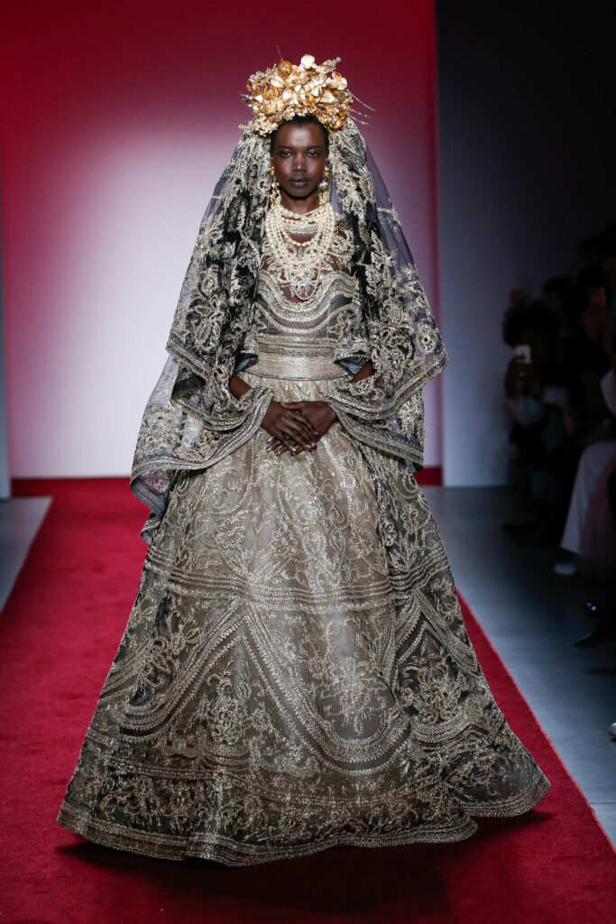 A woman in ornate gown and veil on a runway