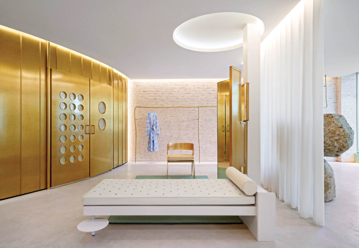 a white chaise sits across from a brass paneled wall