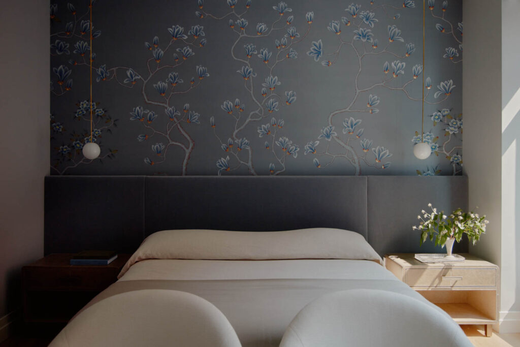a dark blue upholstered headboard against a similar colored floral wallpaper